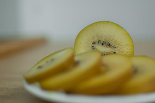 Slices of golden kiwi with yellow pulp on white plate on the kitchen. Exotic fruits, healthy eating concept.