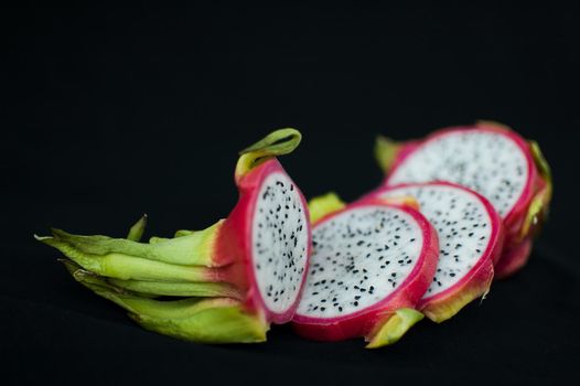 Slices of dragon fruit or pitaya with pink skin and white pulp with seeds on black background. Exotic fruits, healthy eating concept.