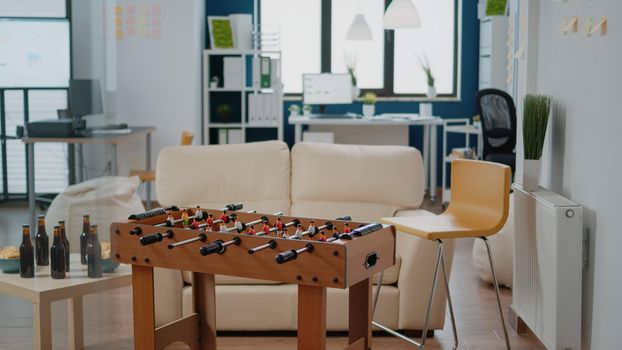 Nobody in workplace for businesspeople meeting after work for drinks and party celebration. Empty office with football game table, snacks and bottles with alcoholic beverage for fun