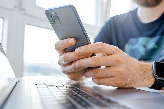 bearded young man picks up something on his phone while working for a laptop . High quality photo