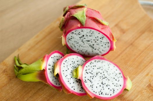 Slices of dragon fruit or pitaya with pink skin and white pulp with black seeds on wooden cut board on the kitchen. Exotic fruits, healthy eating concept.