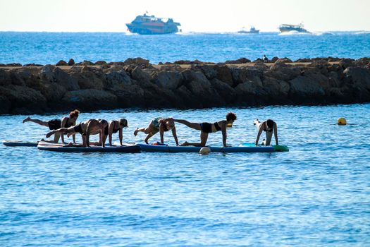 Santa Pola, Alicante, Spain- October 16, 2021: Group of people doing yoga on surfboard on a sunny day of Autumn in Spain