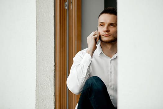 A man sits on an open window, looks at the street and talks on the phone. High quality photo