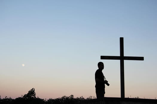 Silhouette of tourist takes photos with a cross on the foreground