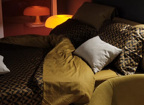 Lamp on a bedside table next to a bed with pillow. night time - wake up and warmth of home concept