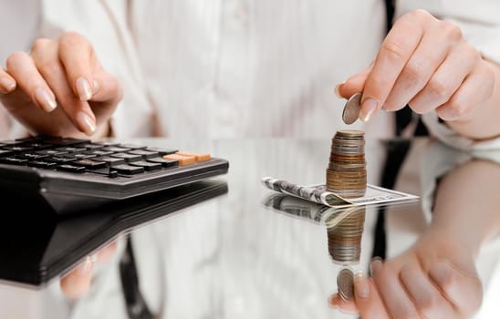 A woman in a white shirt counts coins in a stack on a calculator . High quality photo