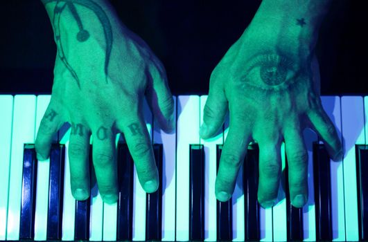 Tattooed mans hands on the keyboard of a piano. Dark background