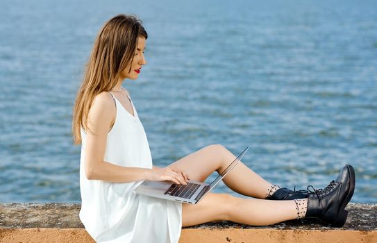 Businesswoman comfortably positioned on a concrete fence berth works behind a laptop . High quality photo