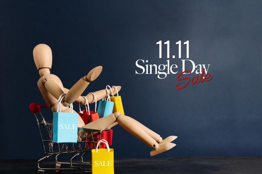 11.11 singles day sale concept, shopaholic wooden doll with lots of shopping bags on arm and shopping cart