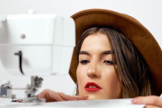 Cute girl in hat uses sewing machine sews paper High quality photo