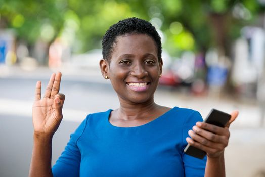 young girl standing in blue camisole cellphone in hand watching the camera smiling.
