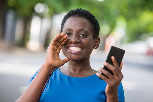 young girl standing in blue camisole cellphone in hand watching the camera smiling.