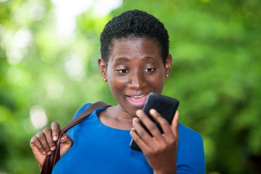 young girl standing in blue camisole looking at mobile phone while smiling.