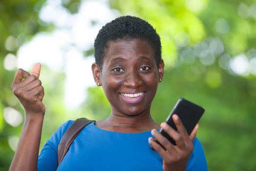 young girl standing in blue camisole cellphone in hand watching the camera smiling.