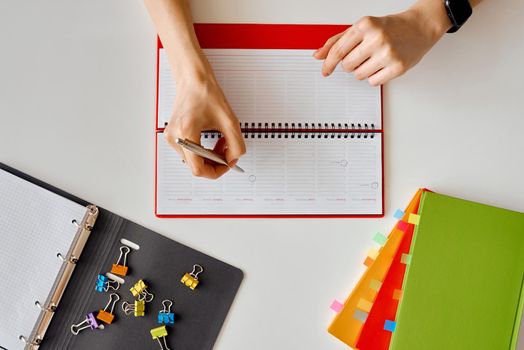 A woman makes a record in a diary on a spring. Desktop with colored notebooks with bookmarks and paper clips. High quality photo