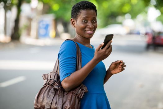 young girl standing in blue camisole with mobile phone looks at camera smiling.