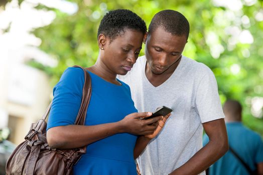 young couple standing staring at mobile phone.