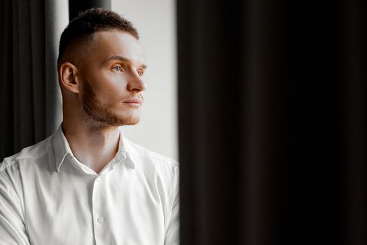 young man in white shirt stares to the left side of the window. High quality photo