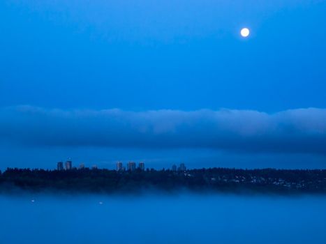 Night city in clouds with full moon over in the sky.