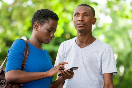 young girl standing in blue camisole looking at her cell phone while her friend looks in front of him with strange air.