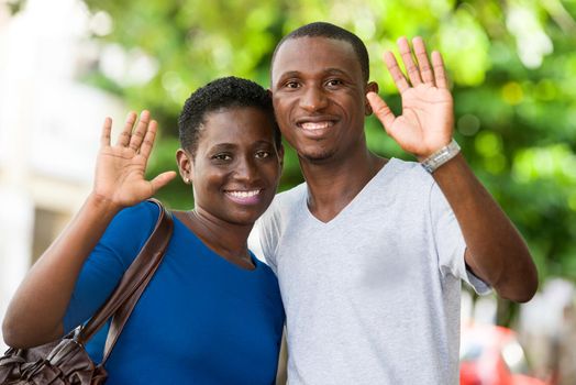 young couple standing hands raised looks at camera smiling.