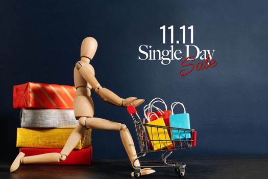 11.11 singles day sale concept, shopaholic wooden doll with lots of shopping bags on arm and shopping cart