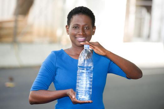 Happy woman shows a large bottle of mineral water standing alone outdoors in a sunny day