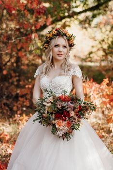 blonde girl in a wedding dress in the autumn forest against the background of wild red grapes