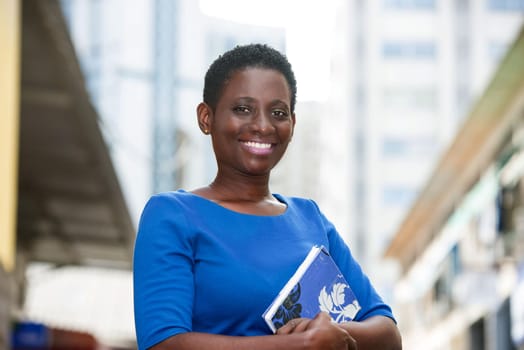 young student standing in blue camisole with book glued to the chest looks at the camera smiling.