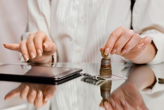 A woman counts finances on a tablet holding a coin from a stack on a banknote . High quality photo