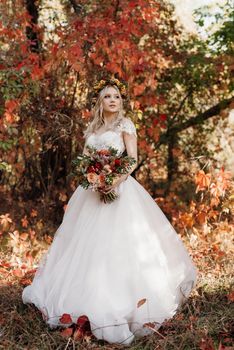 blonde girl in a wedding dress in the autumn forest against the background of wild red grapes