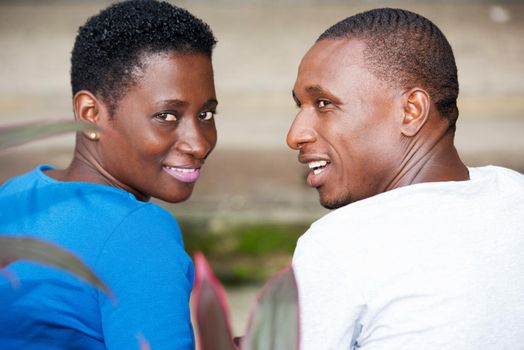 young couple sitting in park and looking from behind the camera smiling.