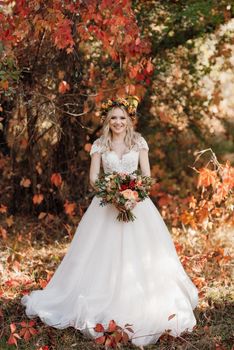 blonde girl in a wedding dress in the autumn forest against the background of wild red grapes