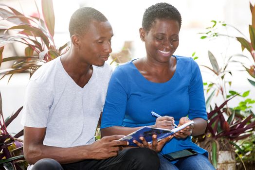 young girl sitting beside her friend having something to note in notebook smiling.