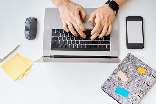 A man types text, works behind a laptop, next to a phone with a white crane . High quality photo