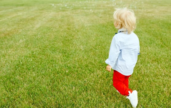 Uncertain boy runs away on green grass. High quality photo