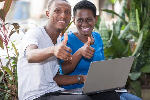 young students sitting in park with laptop wave fingers smiling on camera.