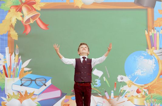 first day of school the boy stands in front of the board with his hands up. High quality photo