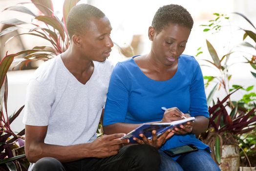 young girl sitting next to her friend writing something in a notebook.