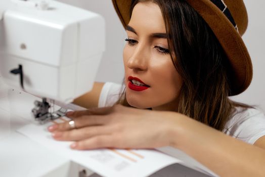 Cute girl in hat uses sewing machine sews paper High quality photo