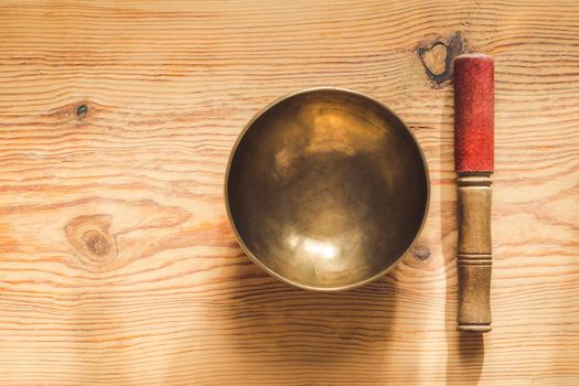 Tibetan copper bowl and wooden stick on wooden table with copy space.