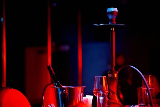 classic hookah on the table in blue and red light with glasses and a bucket with wine. High quality photo