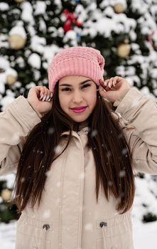 Merry Christmas and happy New Year. Happy Woman in warm winter clothes standing by the big christmas tree outdoors, snow falling