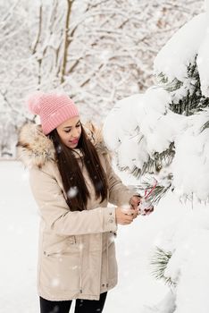 Merry Christmas and happy New Year. Beautiful woman in warm winter clothes decorating Christmas tree in a park in snowy day