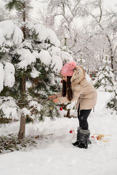 Merry Christmas and happy New Year. Beautiful woman in warm winter clothes decorating Christmas tree in a park in snowy day