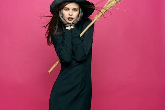 woman in black suit witch broomstick posing pink background. High quality photo