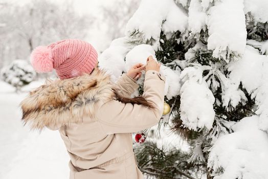 Merry Christmas and happy New Year. Beautiful woman in warm winter clothes decorating Christmas tree in a park in snowy day