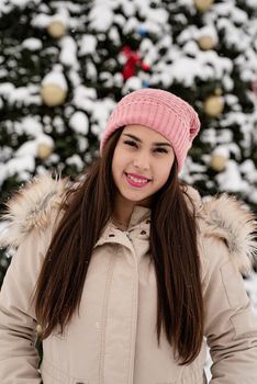 Merry Christmas and happy New Year. Happy Woman in warm winter clothes standing by the big christmas tree outdoors, snow falling