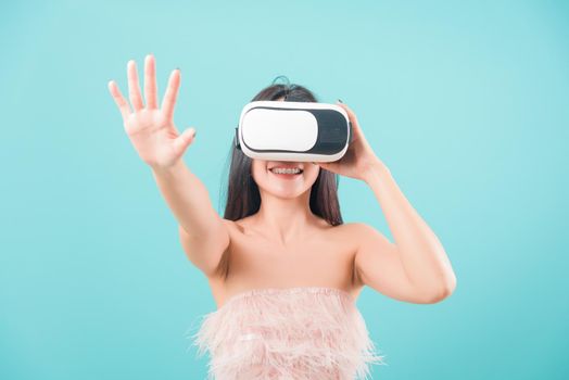 Asian happy portrait beautiful young woman standing smile her using a virtual reality headset, playing on VR glasses device on blue background with copy space for text