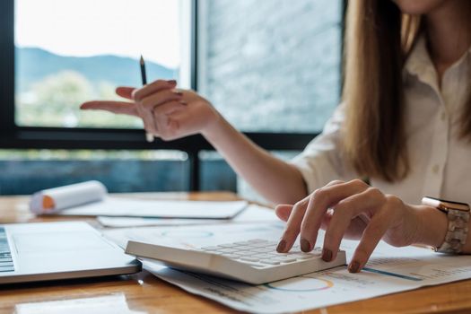 Business woman working in finance and accounting Analyze financial budget with calculator and laptop computer in the office.